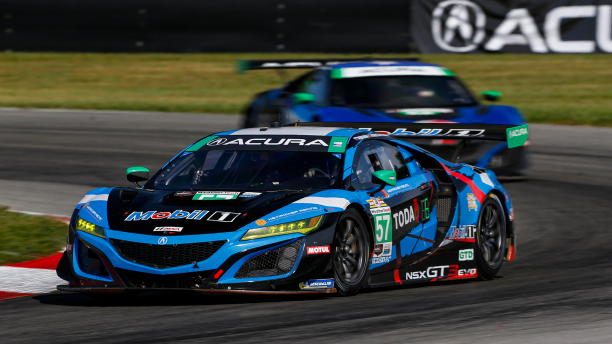 Head-on view of two blue Acura race cars speeding around the bend of a track, one in front of the other. Vue avant de deux voitures de course Acura bleues l’une derrière l’autre qui négocient une courbe sur un circuit de course.
