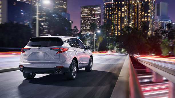 An Acura RDX drives through a city at night. / Un Acura RDX roulant dans une ville la nuit.